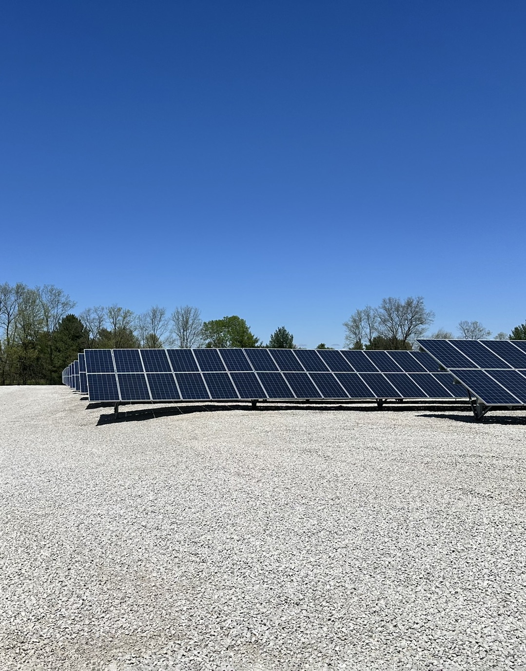 Solar Panel Array in Clear Sky Rows of solar panels installed on a gravel surface under a clear blue sky.